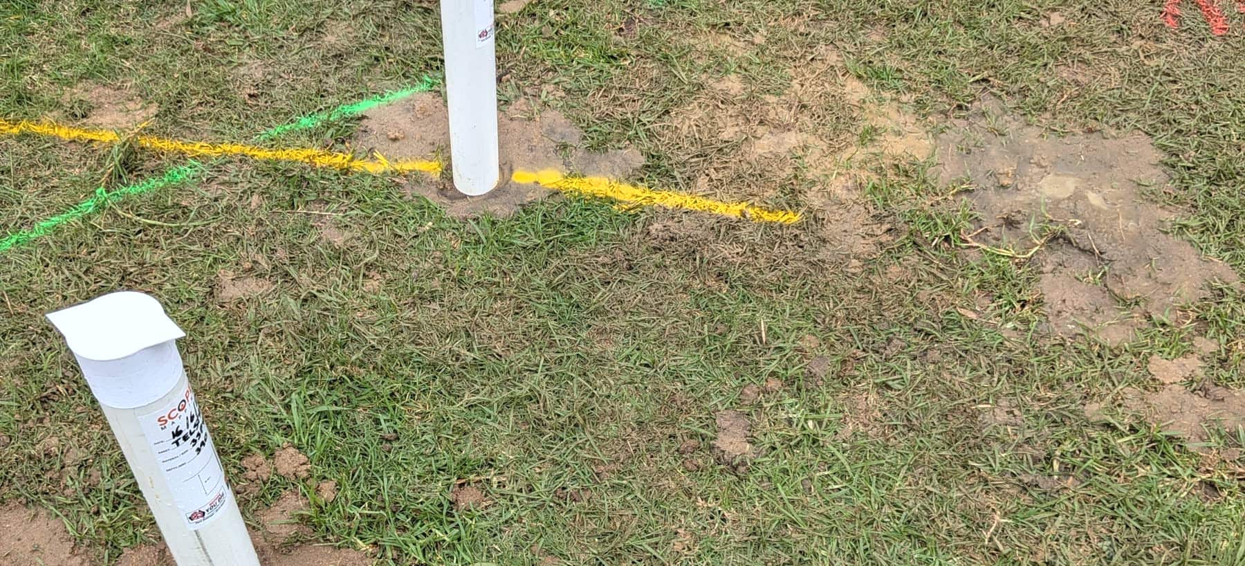 Underground services marked out on grass with spray lines and a Scope Mapping marker post
