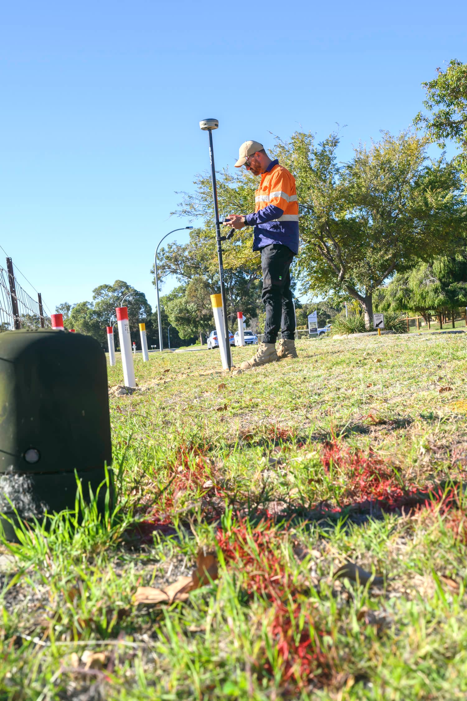 A Scope Mapping locator recording a located service with a GNSS rover beside marker posts on a Perth verge